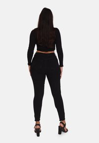 Jeans skinny negros de tiro alto con un acabado texturizado, con bolsillos traseros y un dobladillo deshilachado. Combinados con sandalias negras de tacón cuadrado.