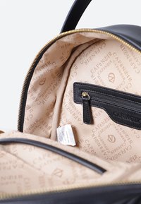 Svart läderväska med en beige foder med ett upprepat logomönster. Inkluderar en ficka med blixtlås och gyllene blixtlåsdetaljer.