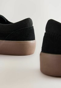 Scarpe nere in suede e tessuto con una finitura opaca testurizzata, dotate di una suola in gomma marrone e accenti di cucitura in contrasto.