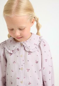 Blusa viola chiaro in tessuto strutturato con colletto a volant, piccoli motivi floreali e chiusura frontale a bottoni. Maniche lunghe a palloncino.