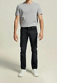 Graues T-Shirt mit kurzen Ärmeln, kombiniert mit schwarzen Denim-Jeans und weißen Turnschuhen, vor neutralem Hintergrund präsentiert. Legere Kleidung, schlichtes Design.