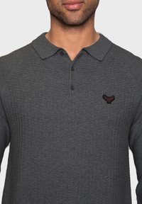Graues langärmliges Poloshirt mit strukturierter Oberfläche, mit einem Kragen, drei Knöpfen und einem kleinen bestickten Logo auf der Brust.