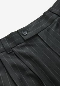 Pantalons noirs à rayures avec une texture lisse, dotés d'une fermeture à bouton à l'avant et de passants de ceinture. Motif en chevrons dans le tissu.