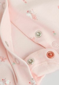 Lyserød bomuldsdragt med blomsterprint, forsynet med sølv-, rosagulds- og hvide trykknapper. Blød tekstur og ribbekrave detaljer.