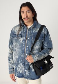 Farkkutakki vaalealla happopesulla, kaksi rintataskua ja nappeja. Musta olkalaukku säädettävällä hihnalla ja logolla.