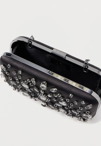 Čierna kabelka na ruku s matným povrchom, zdobená rôznymi kryštálovými ozdobami. Obsahuje strieborný kovový rám a zapínanie.