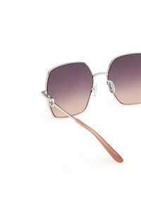 Gafas de sol de forma cuadrada con montura de metal plateado, lentes degradados de púrpura a beige y extremos curvados de varillas en marrón claro sobre fondo blanco.
