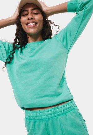 Turquoise sweatshirt met een relaxte pasvorm en een ronde hals, samen met bijpassende joggers met een elastische tailleband. Zachte textuur.