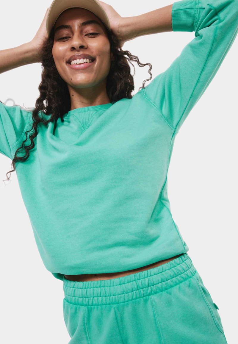 Felpa turchese con vestibilità rilassata e scollatura a girocollo, abbinata a pantaloni joggers coordinati con vita elastica. Texture morbida.