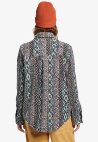 Multicolored flannel shirt featuring a patterned design in soft fabric. Geometric shapes in blues, pinks, and browns. Button-up front, curved hem.