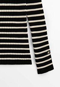 Manche de pull en tricot côtelé à rayures horizontales noires et blanches avec un petit bouton rond doré près du poignet, sur fond blanc.