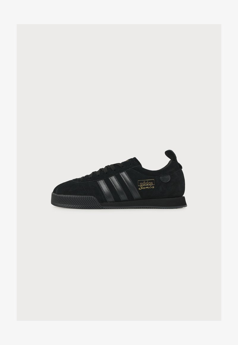 Μαύρο αθλητικό παπούτσι Adidas Samba με μαύρες ρίγες, υφή στη σόλα, χρυσά γράμματα και θηλιά σε απλό λευκό φόντο.