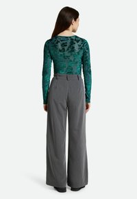 Bodysuit de manga larga con estampado floral verde y textura transparente, combinado con pantalones de pierna ancha grises de cintura alta.