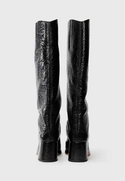 Botas negras hasta la rodilla con un material de cuero texturizado, puntera cuadrada y tacón grueso, con costuras visibles a lo largo de la costura trasera.