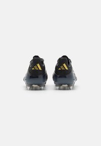 Svarte fotballsko med teksturert overdel, som har en blank mørkeblå såle og en gul tre-stripes logo på hælen. Delt for bedre grep.