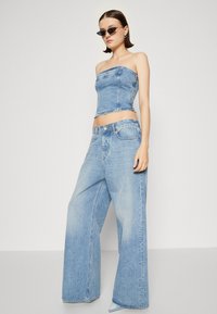 Ensemble en denim bleu clair en deux pièces comprenant un crop top sans bretelles et un pantalon large. Texture lisse, coutures en denim classiques, design décontracté.