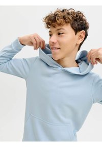 Sudadera azul claro con capucha y bolsillo frontal, presenta una textura suave y un ajuste relajado, llevada con la capucha bajada.