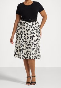 Svart kortärmad topp i kombination med en knä-lång krämfärgad kjol med svart blommönster, åtdragen i midjan med ett svart bälte.