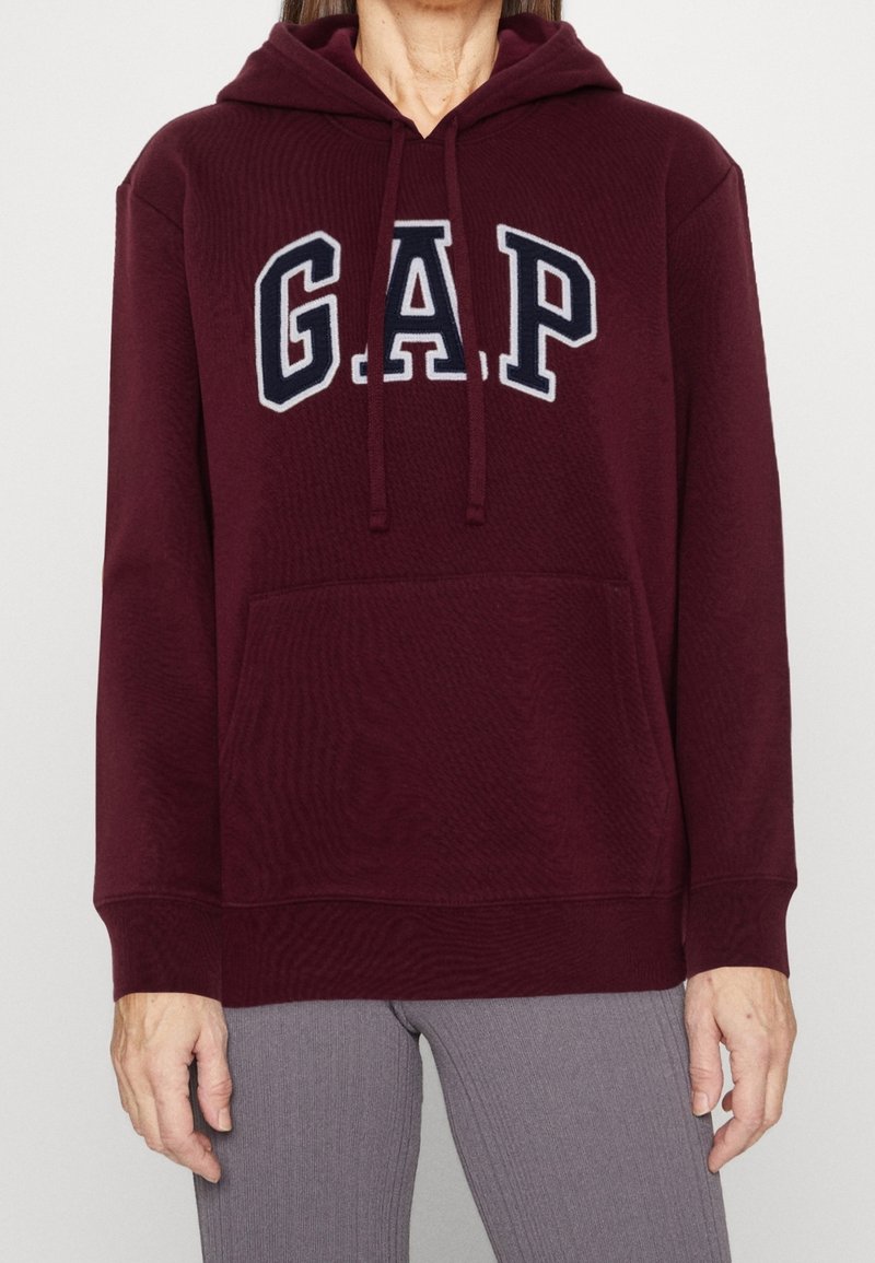 Sweat à capuche bourgogne avec un grand logo "GAP" en bleu marine, capuche à cordon de serrage, poche avant, bords côtelés aux poignets et à l'ourlet, et une texture douce.