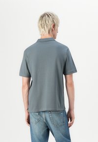 Grå kortærmet polo skjorte med krave, lavet af glat stof. Har en afslappet pasform og slidser i siderne ved kanten, parret med blå jeans.