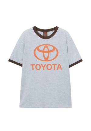 Szara bawełniana koszulka z brązowym ściągaczem u kołnierzyka i na rękawach. Z przodu umieszczono pomarańczowe logo Toyoty oraz tekst na środku.