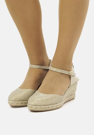 Escadrilles compensées en paillettes dorées avec une semelle intermédiaire en jute tissé et une bride autour de la cheville, présentant un dessus texturé et une zone de orteil lisse.