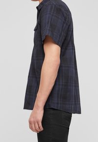 Camicia a maniche corte a quadri in blu scuro e nero, realizzata in tessuto leggero, con colletto button-down e taschino sul petto.