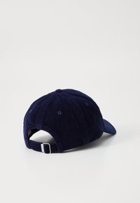Gorra de béisbol de pana azul marino con visera curva, correa ajustable y costura decorativa en la parte trasera. Tela texturada y duradera.