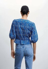 Blusa blu con motivo a fantasia, maniche a sbuffo e orlo peplum, realizzata in tessuto morbido, caratterizzata da motivi floreali bianchi e scollatura rotonda.