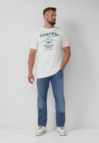 Witte katoenen t-shirt met groene bedrukte tekst en graphics. Gepaard met lichtblauwe denim jeans en witte sneakers. Eenvoudig ontwerp.