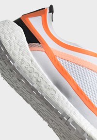 Scarpa atletica bianca con accenti arancioni e tomaia in rete. Suola testurizzata con la scritta "BOOST HD" e un motivo a griglia per la trazione. Design leggero.