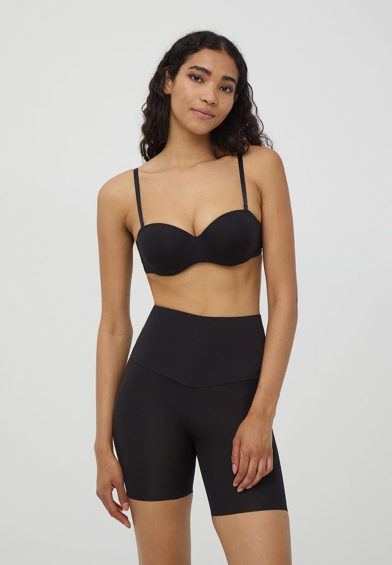 Reggiseno imbottito nero con spalline regolabili, abbinato a pantaloni corti neri a vita alta. Texture liscia, design senza cuciture e stile minimalista.