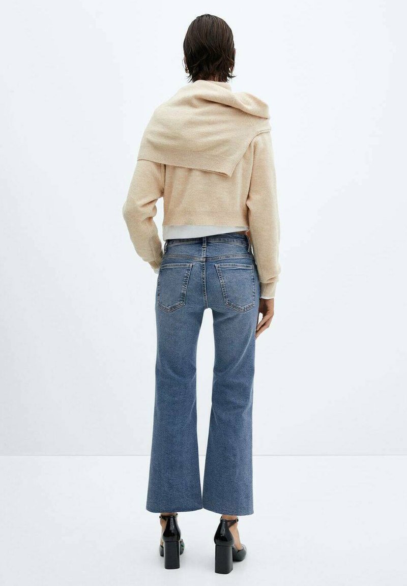 Beige cropped sweater met oversized kraag over de schouders, gecombineerd met lichtblauwe flared jeans en zwarte blokhak schoenen.