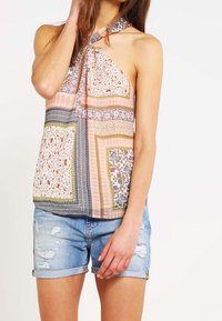 Top con escote halter con patrones de patchwork coloridos en rosa, azul y verde; combinado con pantalones cortos de mezclilla desgastados.