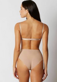 Nude underkläder med en mjuk textur. BH:n har tunna, justerbara band, och de högmidjade trosorna har en vågig kant.