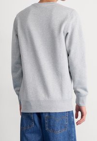 Maglione grigio in cotone con maniche lunghe, scollo rotondo e polsini a costine; texture liscia con vestibilità comoda, abbinato a pantaloncini di jeans.