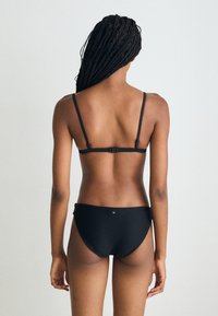Melns bikinis ar regulējamiem siksniņām, aizdari aizmugurē un minimālistisku dizainu. Audumam ir teksturēta ribota struktūra.