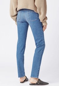 Blue denim jeans with a slim fit, mid-rise waist, and two back pockets. Complemented by a beige knit sweater and black slip-on shoes.