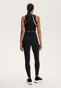 Črn športni crop top in legice z belimi poudarkami. Tkanina ima gladko teksturo, prileganje pa je tesno. Nosi se z črnimi športnimi čevlji.