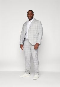 Traje de cuadros grises con una chaqueta entallada y pantalones ajustados. Acompañado de una camisa blanca y zapatillas blancas, creando un aspecto moderno y casual.
