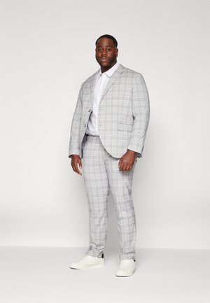 Grau kariertes Anzug mit einem maßgeschneiderten Blazer und eng anliegenden Hosen. Begleitet von einem weißen Hemd und weißen Sneakern, was einen modernen, lässigen Look schafft.