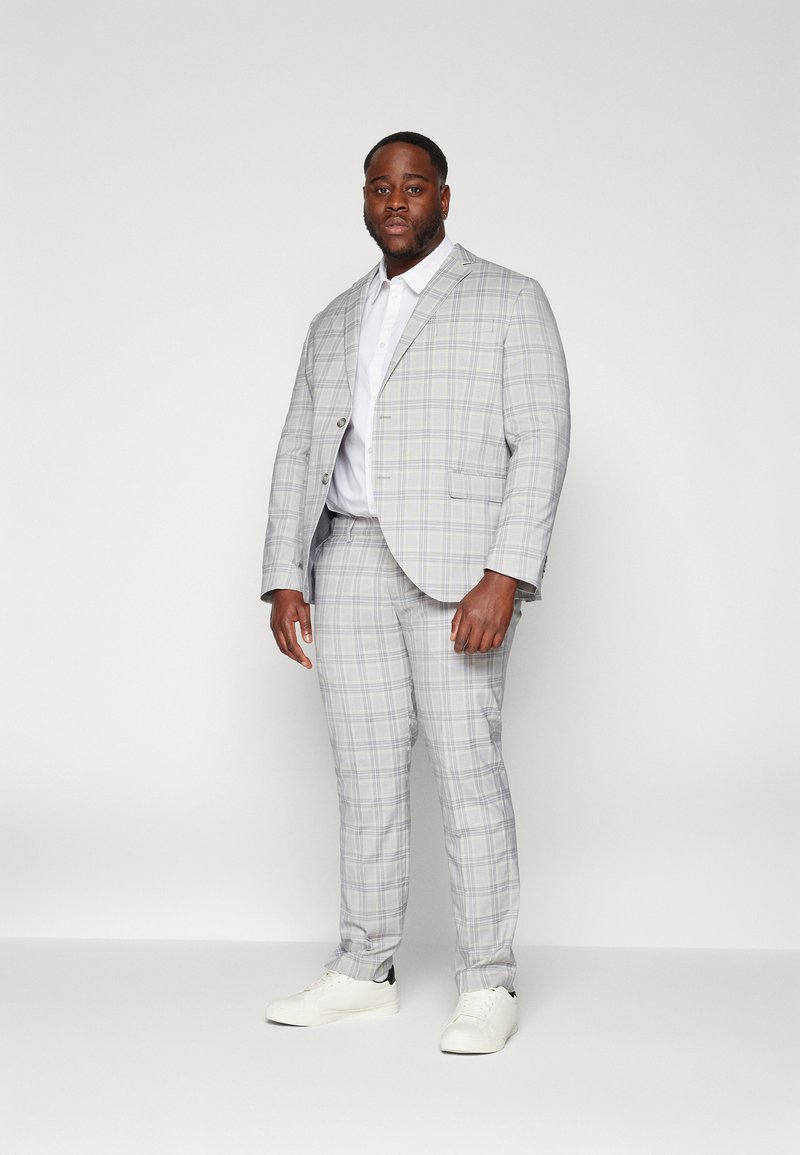 Traje de cuadros grises con una chaqueta entallada y pantalones ajustados. Acompañado de una camisa blanca y zapatillas blancas, creando un aspecto moderno y casual.