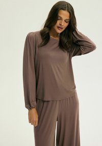 Długosleeve, luźna bluzka z miękkiego, brązowego materiału o gładkiej fakturze i marszczonym mankietami, w komplecie z dopasowanymi luźnymi spodniami.