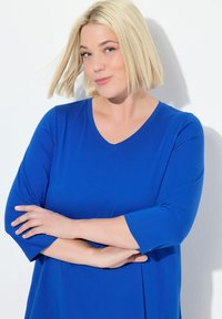 Tunikabluse mit kurzen Ärmeln aus lebhaft blauem Stoff mit weicher Textur und V-Ausschnitt, bietet einen lockeren Sitz für zusätzlichen Komfort.