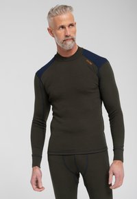 Oliven grøn termisk langærmet skjorte med en tætsiddende pasform, marineblå detaljer på skuldrene og kontrasterende syninger. Stoffet ser tekstureret ud.