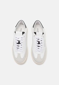 Pari sneakers rendah putih dan abu-abu muda dengan tali sepatu putih dan aksen hitam, dilihat dari atas di latar belakang putih.