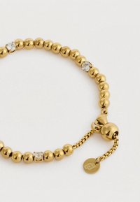 Χρυσό βραχιόλι με χάντρες και τρεις διάφανες πέτρες, ρυθμιζόμενη αλυσίδα και στρογγυλό μοντέρνο κολιέ σε ανοιχτό φόντο.