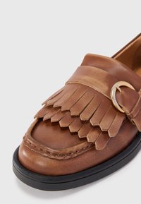 Smeđi kožni loafer s detaljima od fringa, zlatnim hardverskim detaljem i crnom gumenom potplatom. Glatka tekstura s šavnim rubovima.