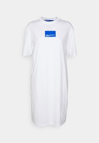 Weißes Baumwoll-T-Shirt-Kleid mit kurzen Ärmeln, ausgestattet mit einem blauen rechteckigen Logo-Patch auf der Vorderseite. Glatte, schlichte Struktur.