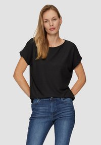 Zwarte top met korte mouwen en een gestructureerde afwerking, ronde halslijn, gecombineerd met slanke blauwe jeans. De top heeft een relaxte pasvorm en subtiele details.